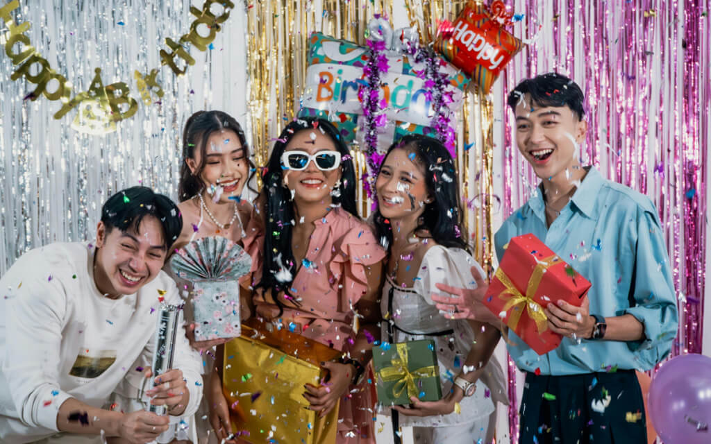 Group of people having fun with confetti falling down around them while holding wrapped gifts